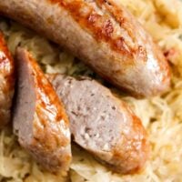 brats with sauerkraut, one sausage sliced, close up on a plate.