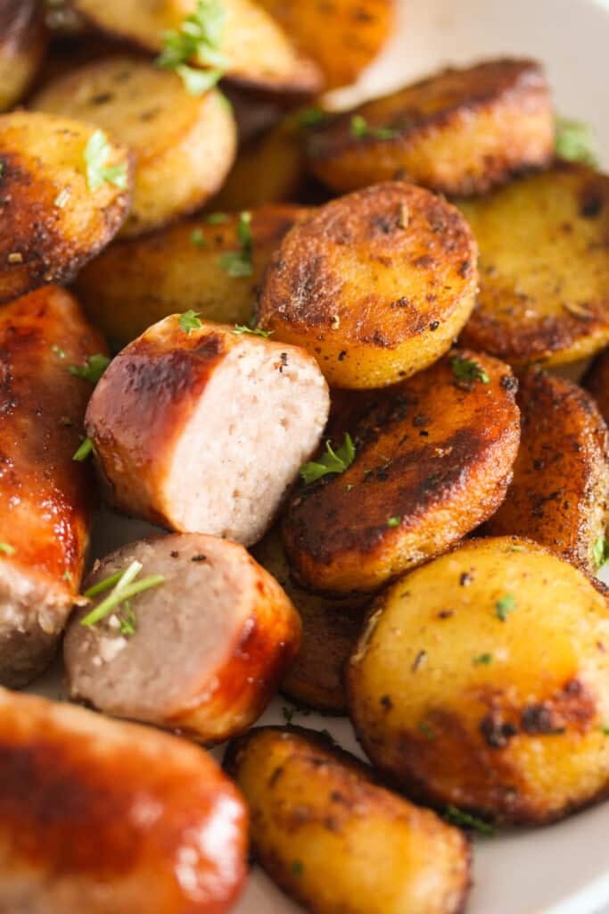close up of fried potato slices and sliced brats sprinkled with parsley.