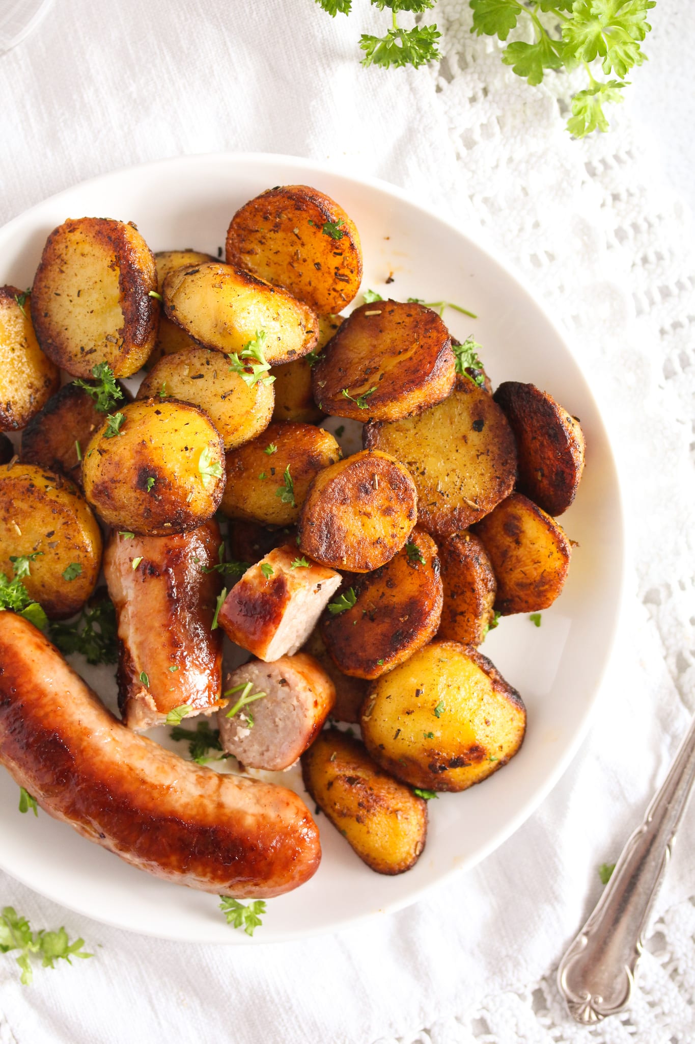 brats and fried potatoes on a small white plate overhead image.