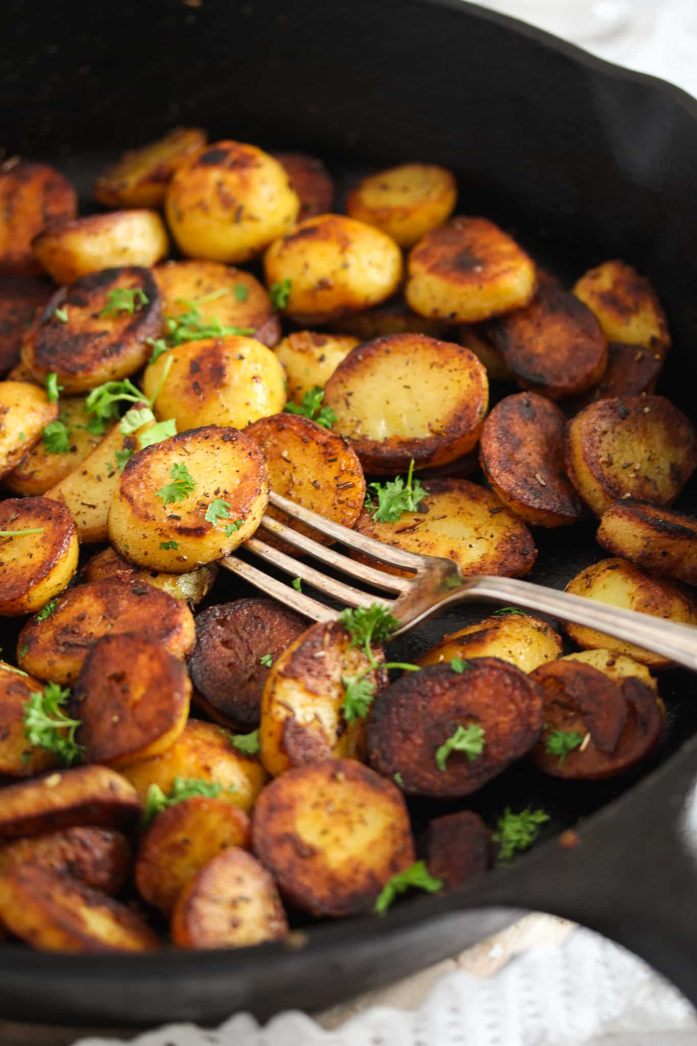 skillet fried potatoes sprinkled with parsley, with a vintage fork.