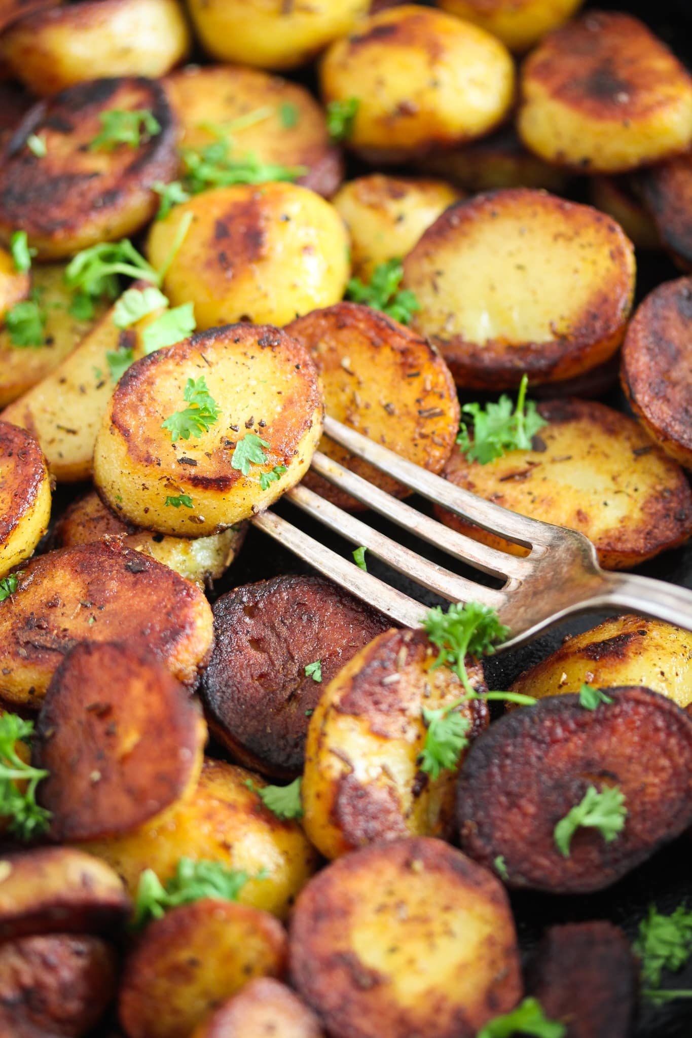 close up golden slices of potatoes fried in pan with a fork on top.