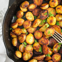 many small potatoes in a heavy-bottomed cast iron pan with a fork.