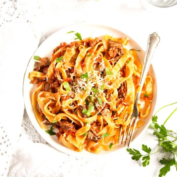slow cooker lamb ragu with pasta on a small white plate with a silver fork.