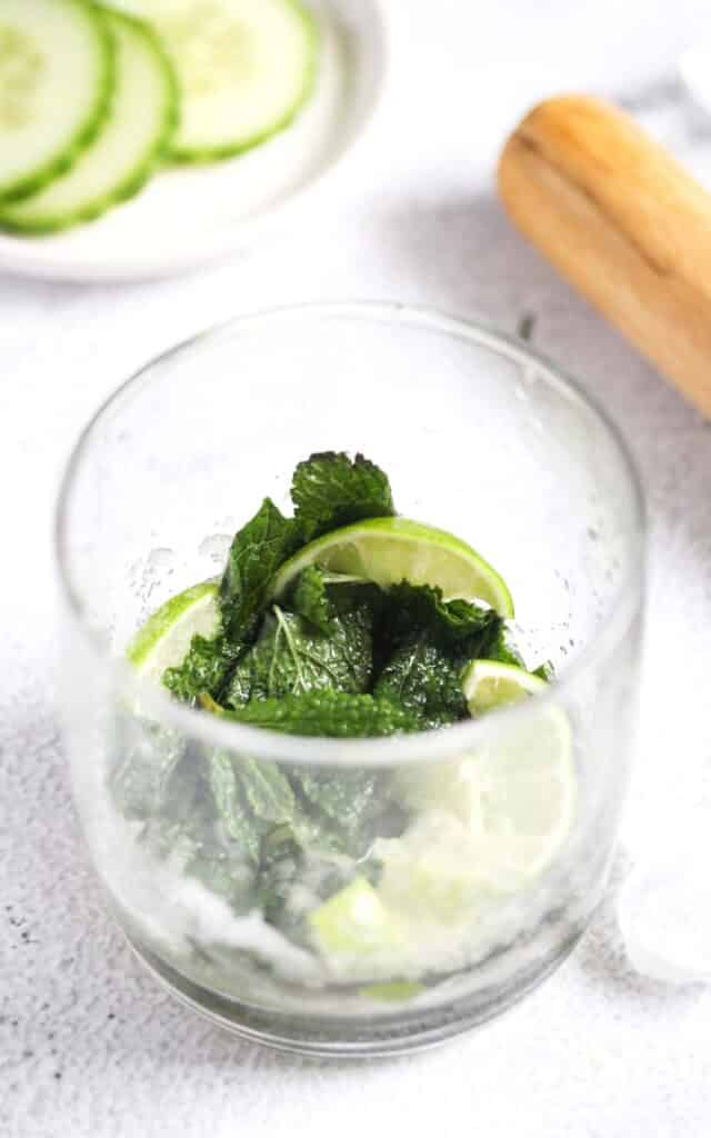 muddled mint leaves and lime slices in a glass.