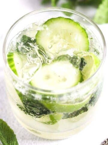glass of gin mojito with cucumber and lime slices.