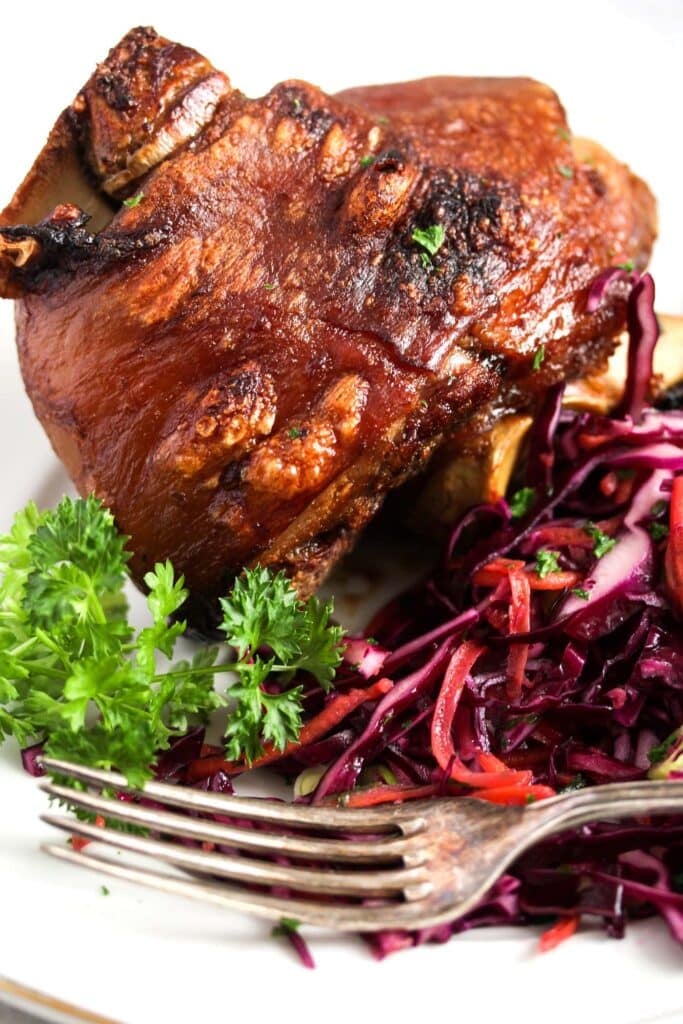 pork knuckle on a plate with red cabbage slaw.