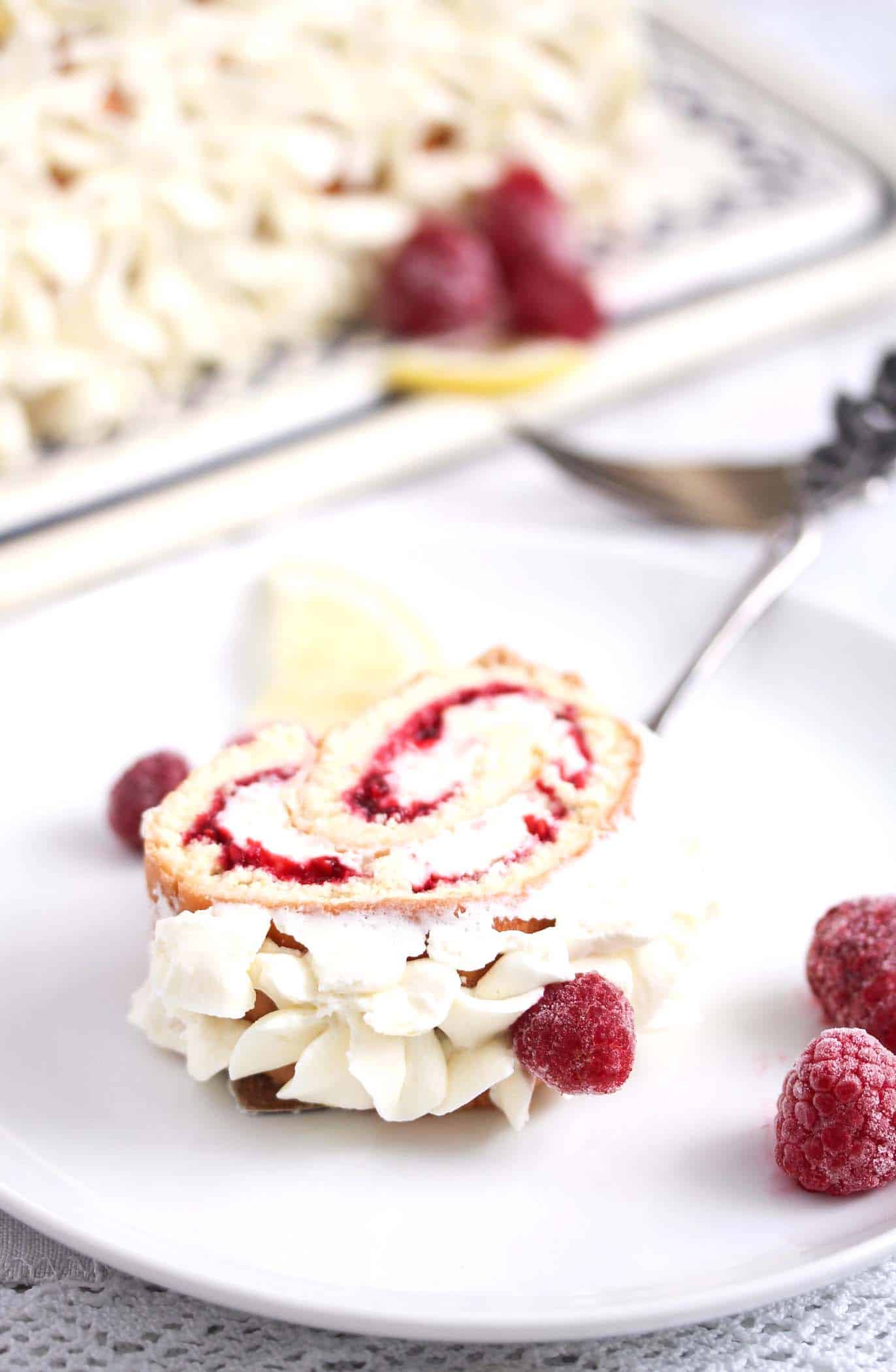 sliced cream roll with raspberries and cream on a plate.