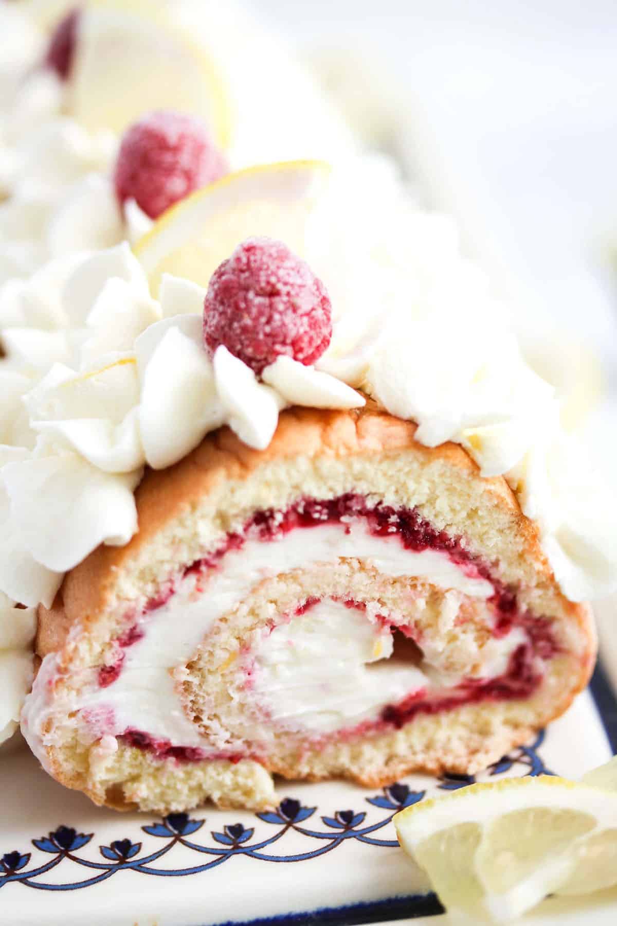 cut raspberry roulade showing the creamy filling, decorated with whipped cream.