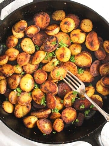 cast-iron skillet potatoes sprinkled with parsley, overhead image.