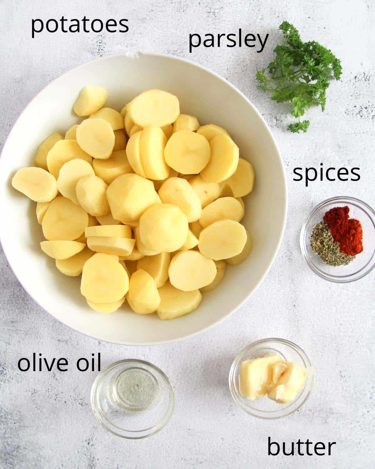 sliced potatoes in a large bowl, fresh parsley, oil, butter and spices in small bowls.