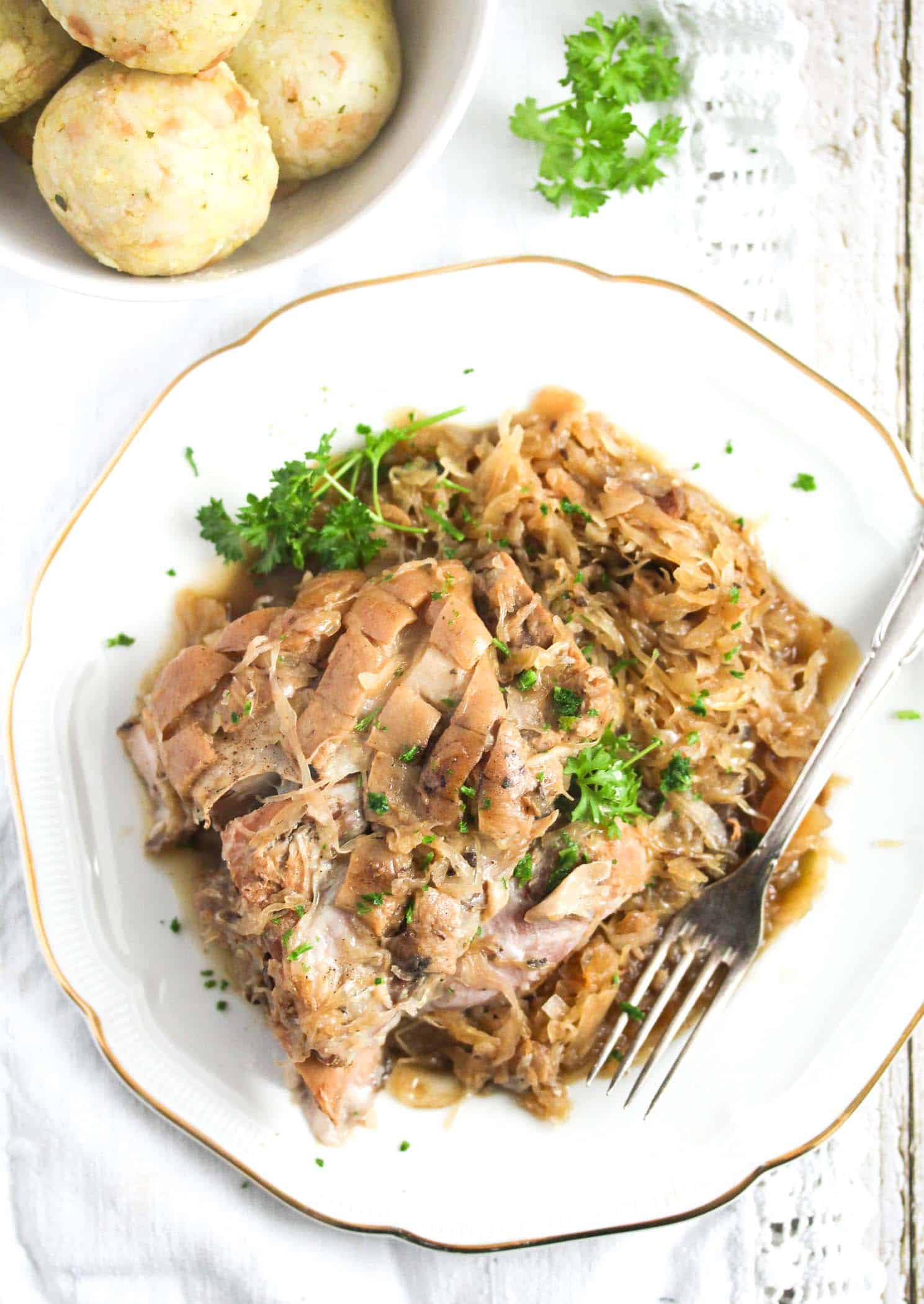 plate with tender pork meat and german kraut sprinkled with parsley.