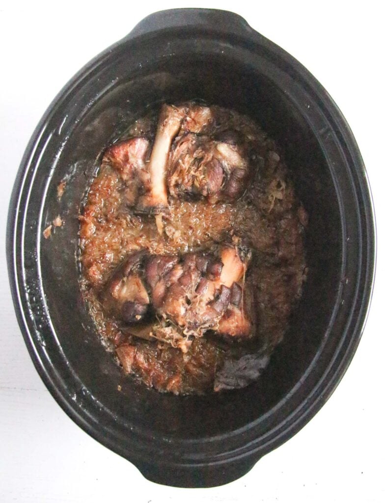 cooked pork hocks with bone showing in a slow cooker.