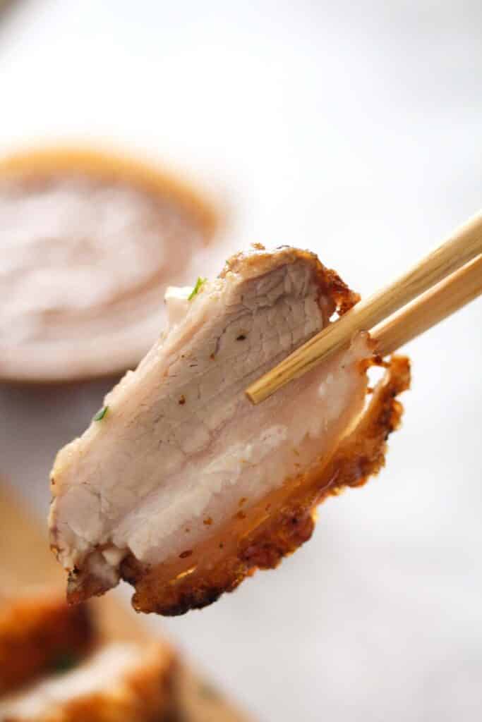 chopsticks holding a piece of crispy pork belly.