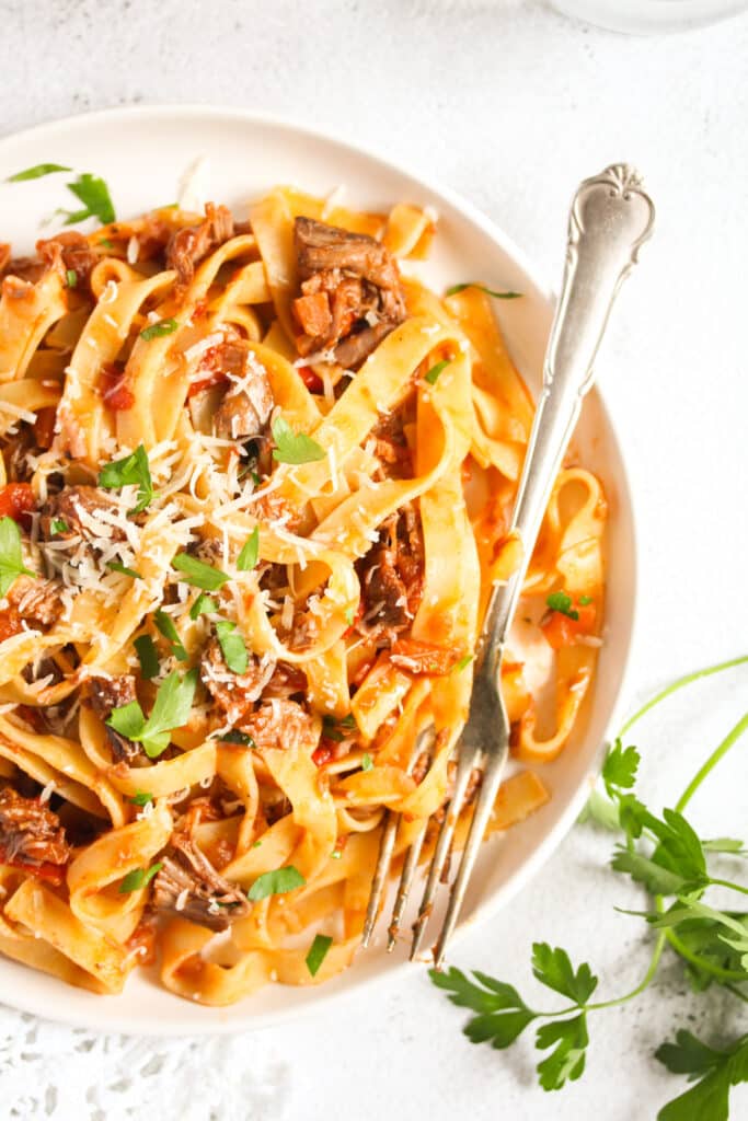 close up pappardelle with lamb ragu on a plate with a fork.