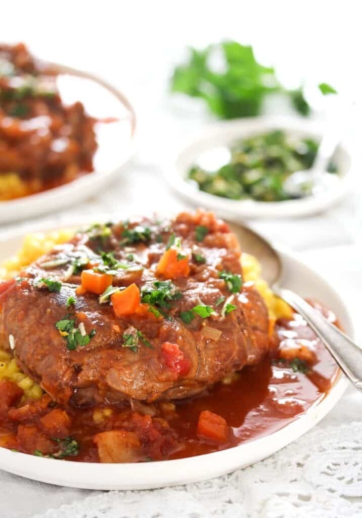 slow cooked osso buco with yellow risotto served in tomato sauce.