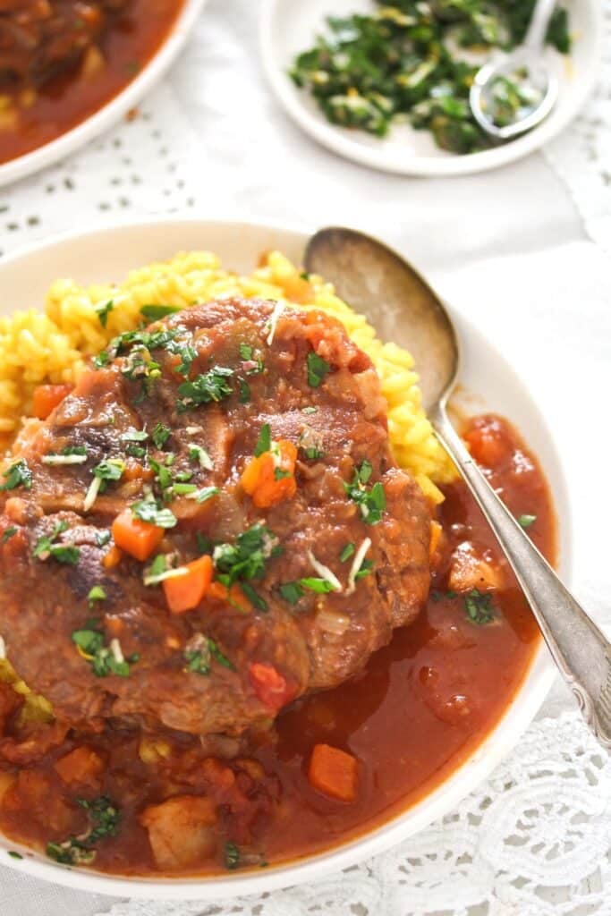 osso buco with risotto milanese and gremolata on a plate.
