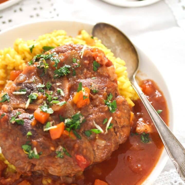 osso buco with risotto milanese and gremolata on a plate.
