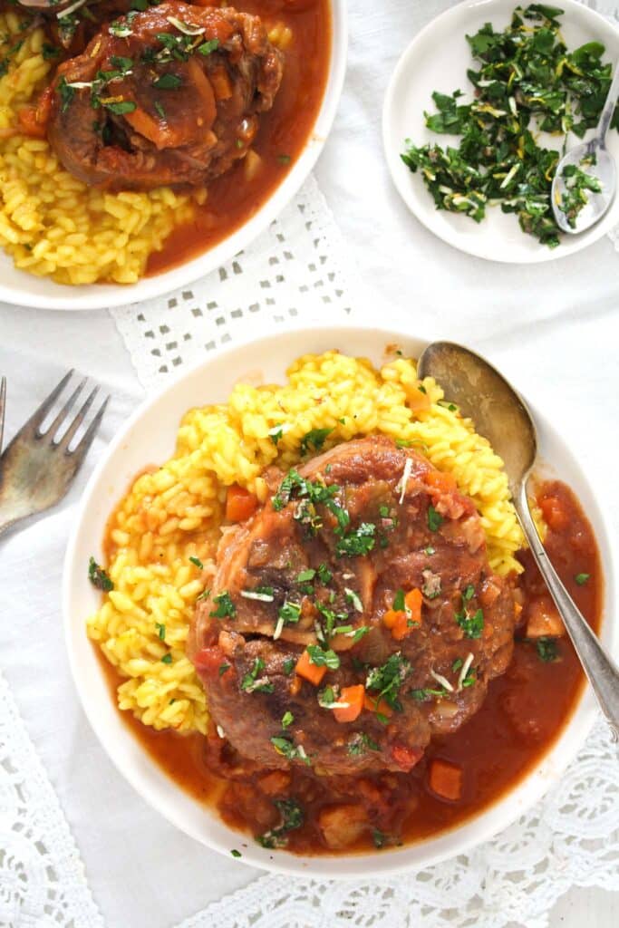 small plates with osso buco served with sauce and risotto milanese. small plate of gremolata beside.