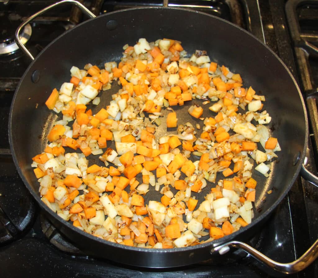 cooking diced carrots, celeriac, onions in a black pan.
