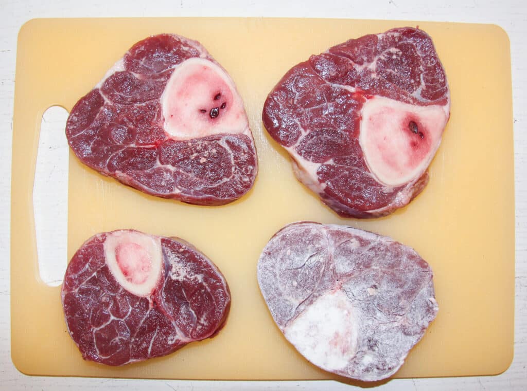four slices of veal shank on a cutting board, one of them floured. 
