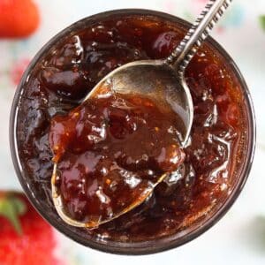 glossy strawberry rhubarb jam without pectin being scooped with a spoon from a jar.