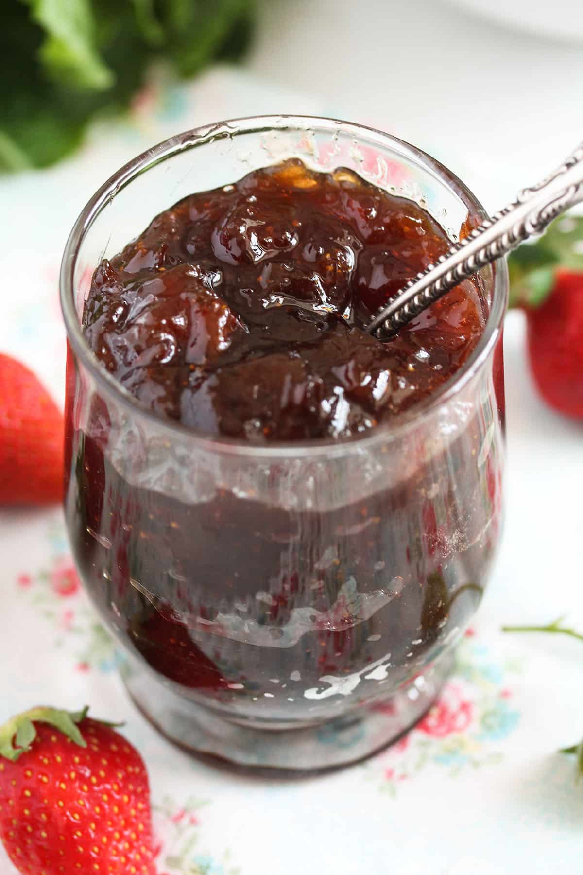 glossy red jam in a small glass with a spoon in it.