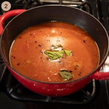 simmering tomato soup with lime leaves on top in a large pot.