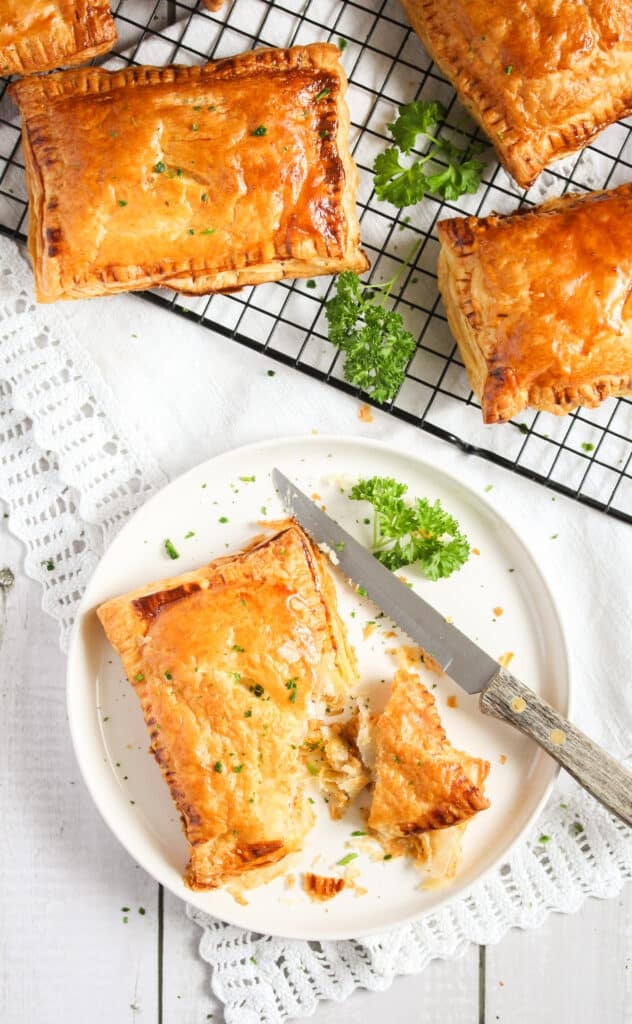 large onion cheddar pasties on a wire rack with parsley, one split on a plate with a knife.