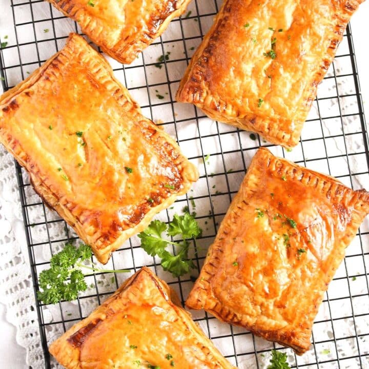 large cheese and onion pasties cooling on a wire rack with a few sprigs of parsley between them.
