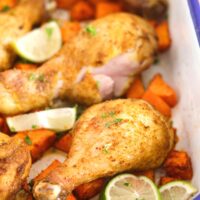 roasting tin with blue rim and chicken legs with potatoes inside.