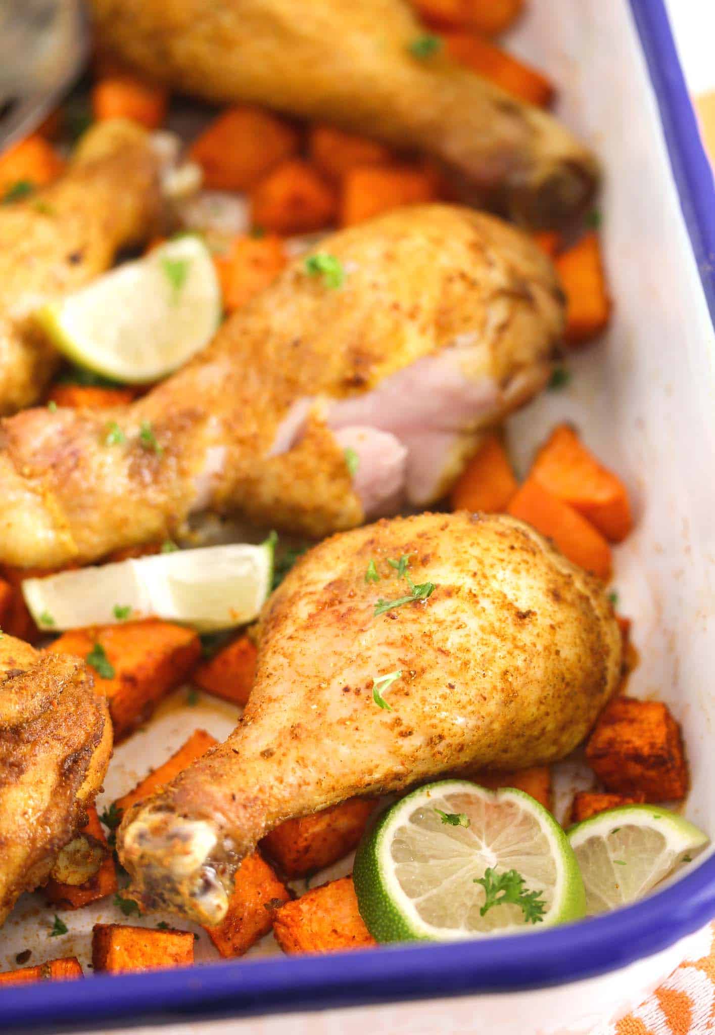 roasting tin with blue rim and chicken legs with potatoes inside.