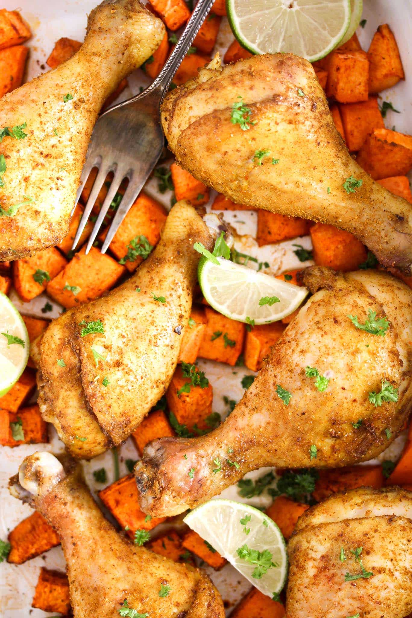 close up of curry chicken drumsticks with lime wedges, sweet potatoes and lime.