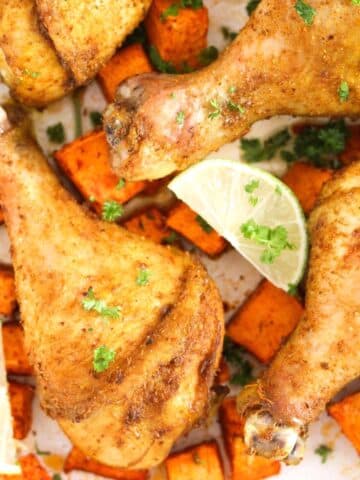 several curry drumsticks with sweet potato pieces and lime wedges in between.