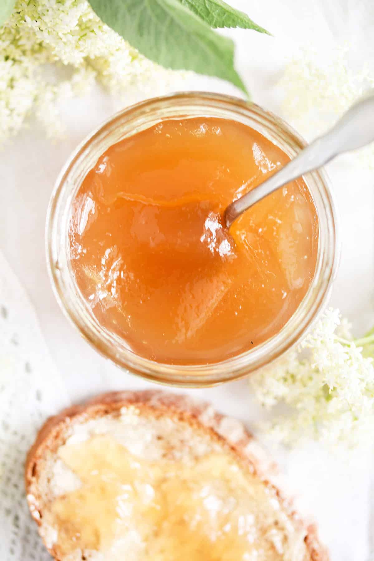 elderflower jam in a jar and a bread slice spread with it.