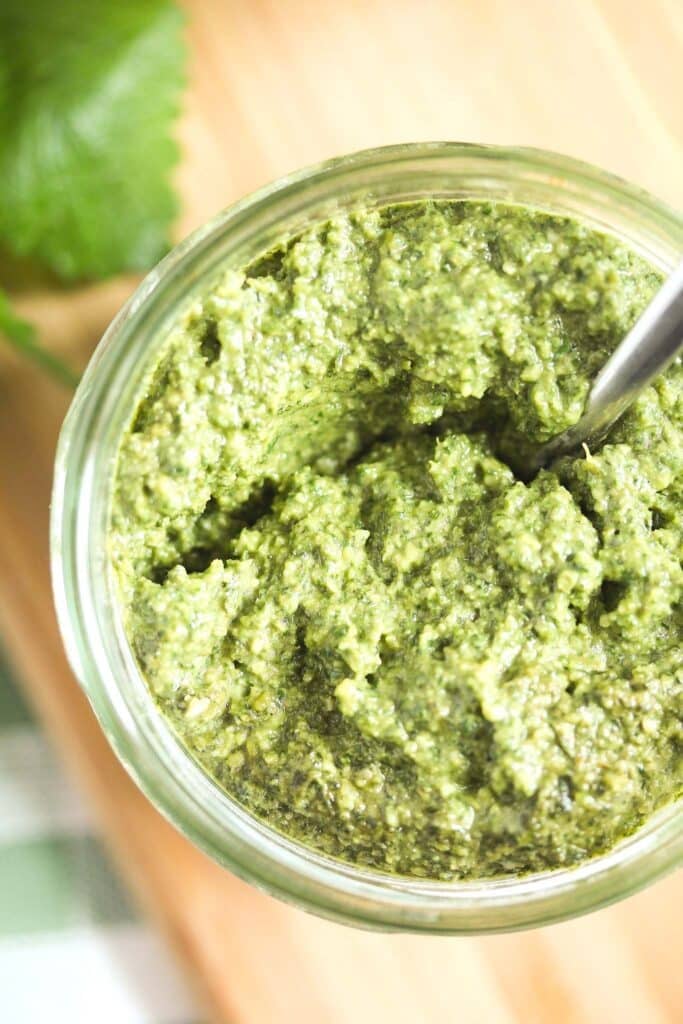 close up of a jar of herb pesto seen from above on a cutting board.