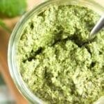 pinterest image of a jar of pesto with a spoon in it on a wooden board.