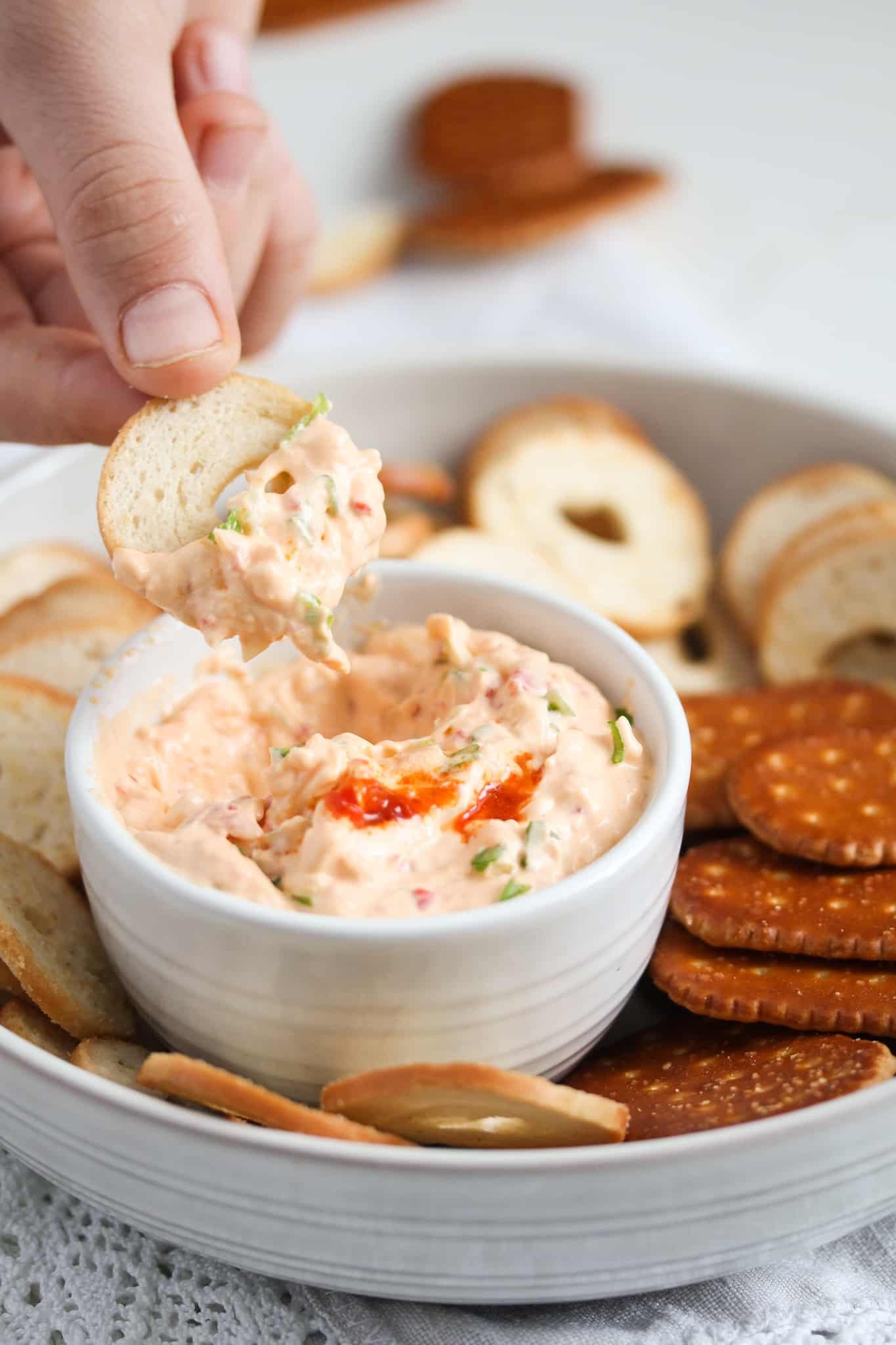 peri peri dip in a small bowl and a hand dipping a cracker in it.