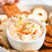 dipping a large salted cracker in cream cheese dip with green onions.