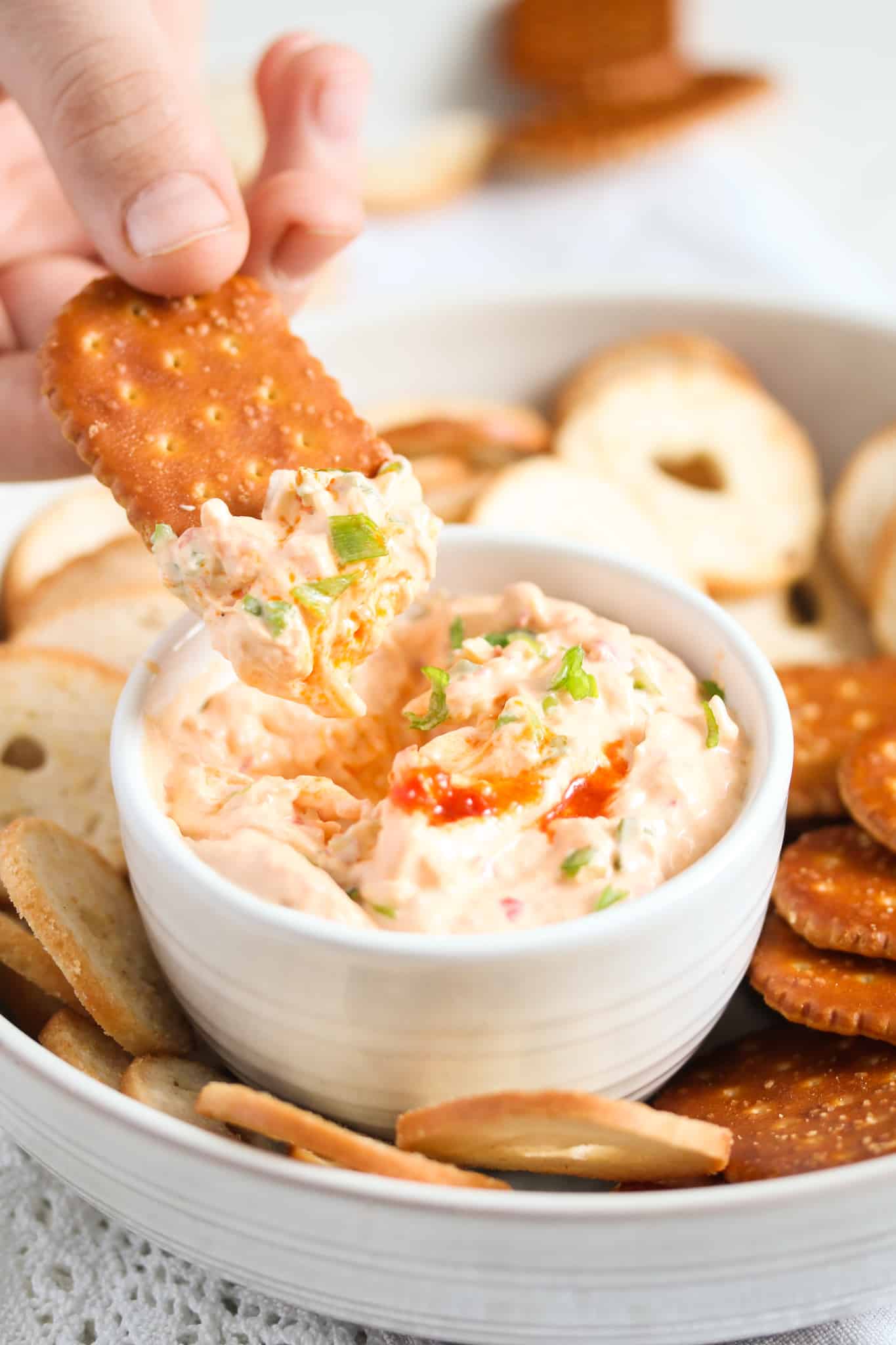 dipping a large salted cracker in cream cheese dip with green onions.