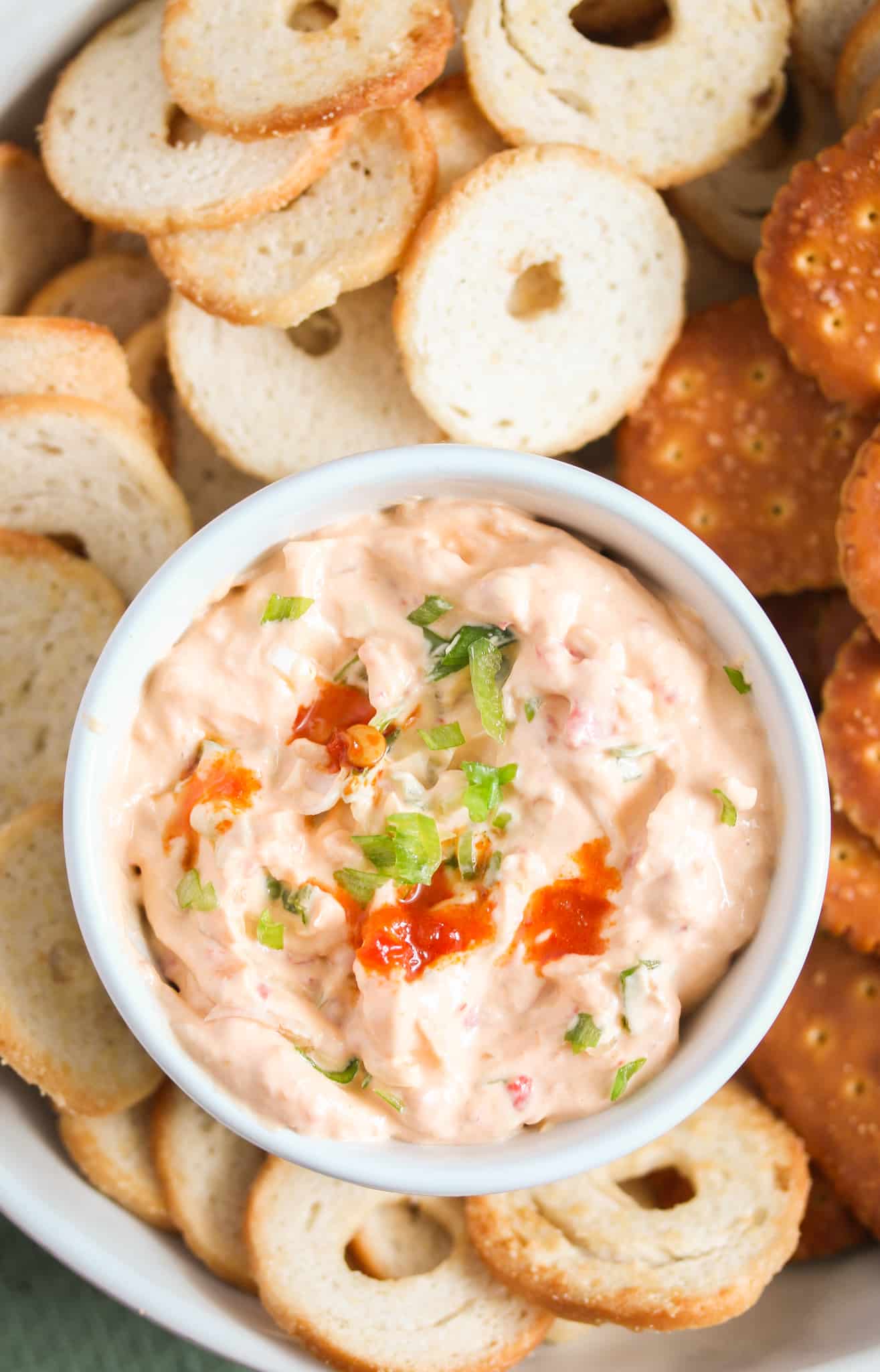 overhead image of a bowl of cold chili dip with crackers all around it.