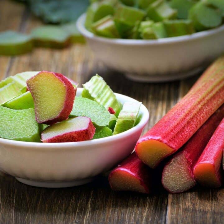 rhubarb stalks and two bowls of chopped rhubarb on a wooden table.