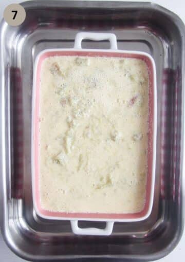 unbaked rhubarb custard in a dish, the baking dish placed in a large one filled with water for bain marie.