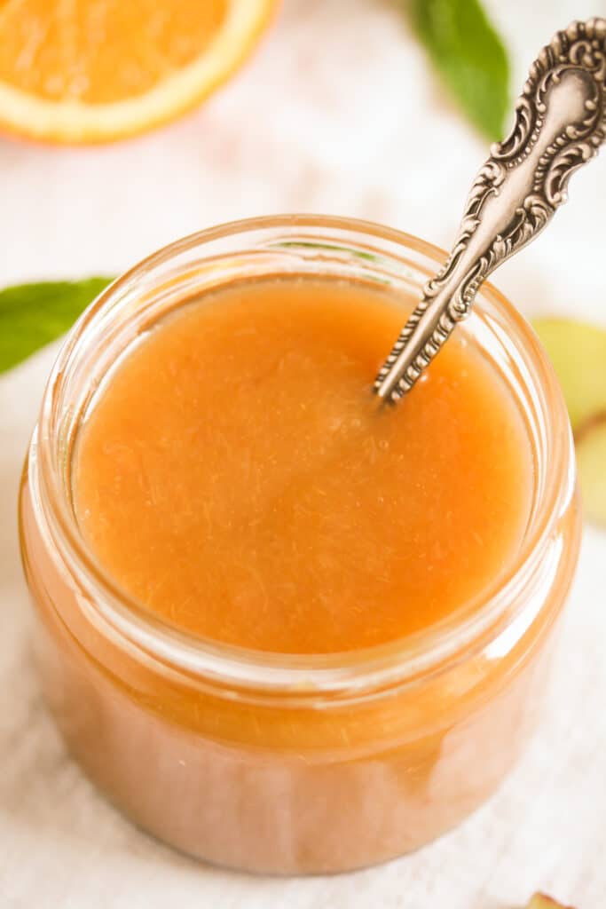 orange jam with rhubarb in a small jar with a spoon in it.
