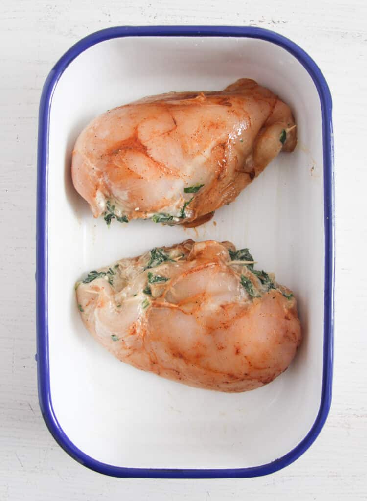 two raw stuffed chicken breasts in a small white baking tin.