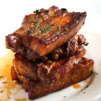 stapled sliced pork belly slices sprinkled with parsley, pool of fat in the back.