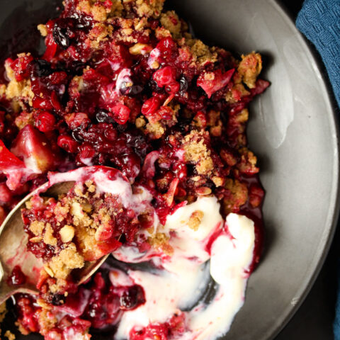 currants and apples covered with crunchy crisp on a black plate with ice cream.