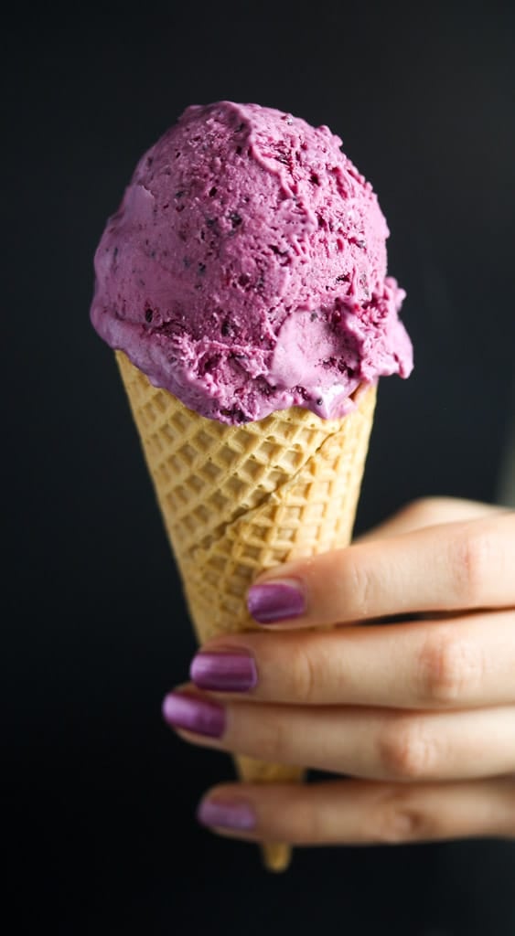 girl's hand with purple colored nails holding a cone of ice of the same color.