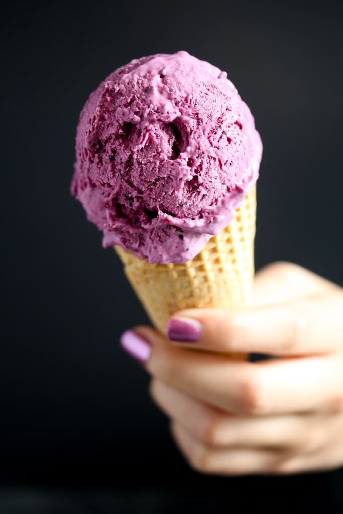 black currant ice cream in a cone held by a girl's hand.