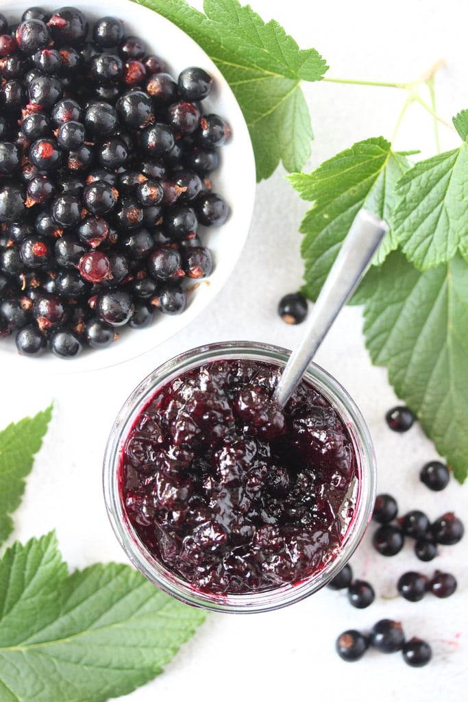 jar of jam and black currants in a bowl, many leaves around them.