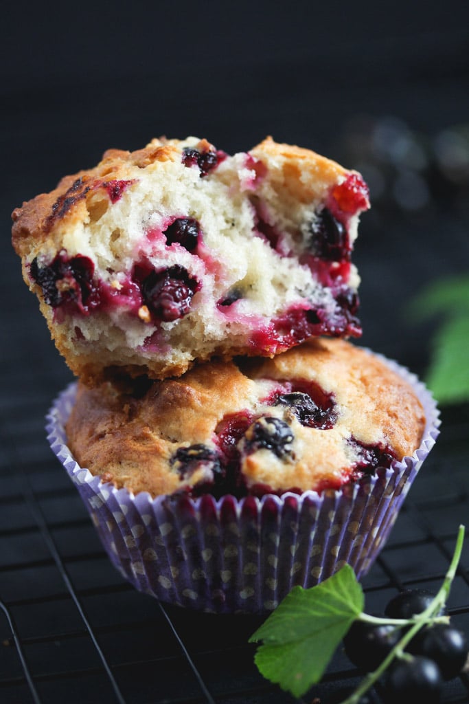 two stapled black currant muffins, one of them split showing the juicy berries inside.